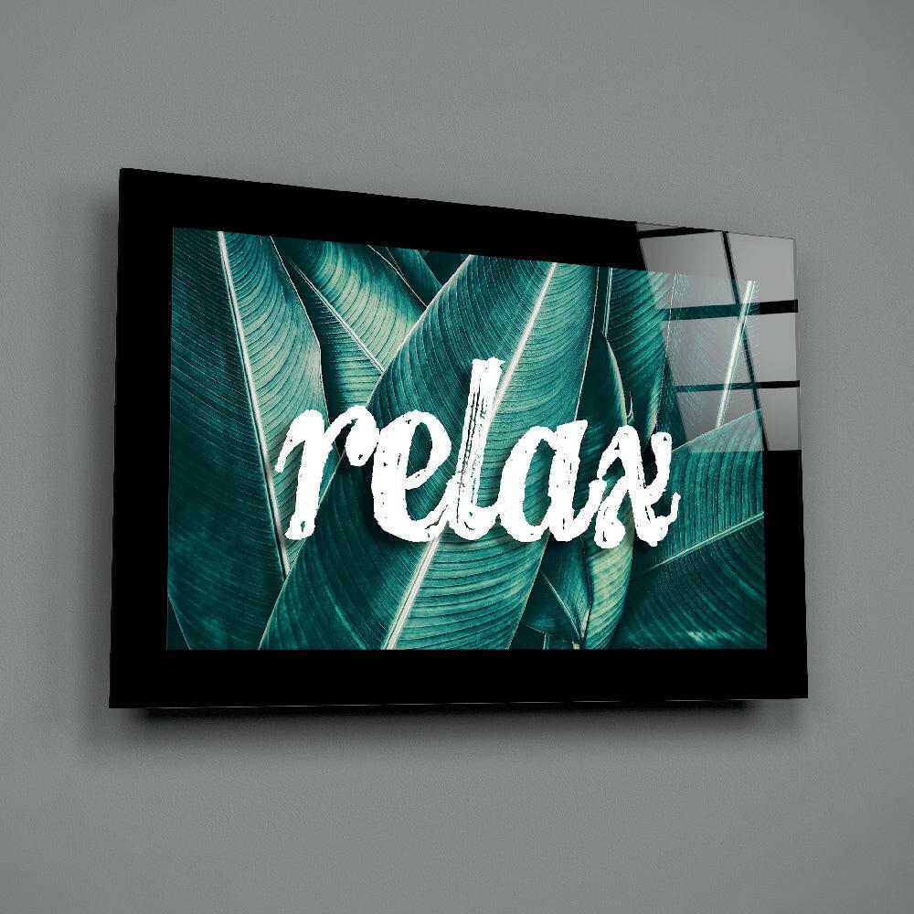 Black-framed glass wall art displaying white "Relax" text over teal tropical leaf background, mounted on gray wall.