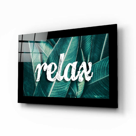 Black-framed glass wall art displaying "relax" text in white over teal tropical leaf background, angled perspective view.