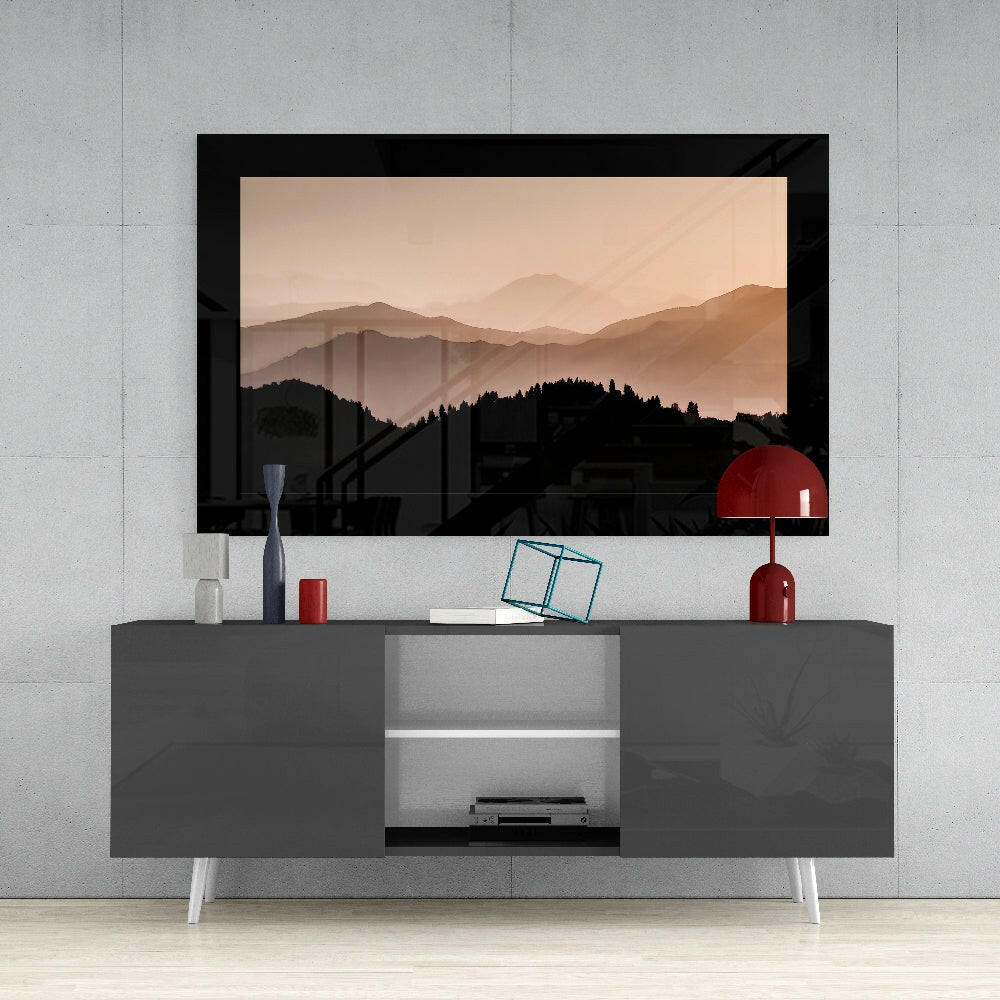 Framed mountain landscape artwork with layered peaks in warm beige and brown tones displayed above gray media console with white legs and red decorative accessories.