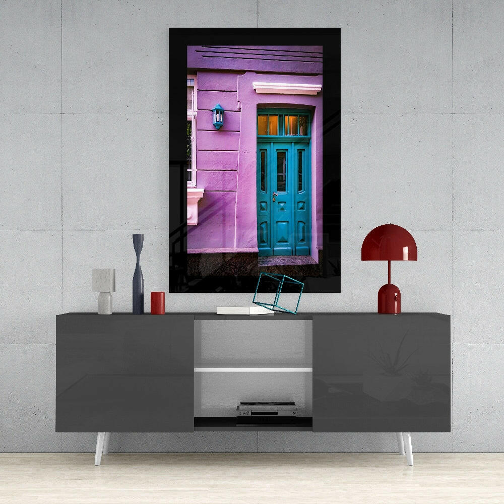 Framed glass wall art depicting a vibrant pink building facade with turquoise door, displayed above a gray media console.