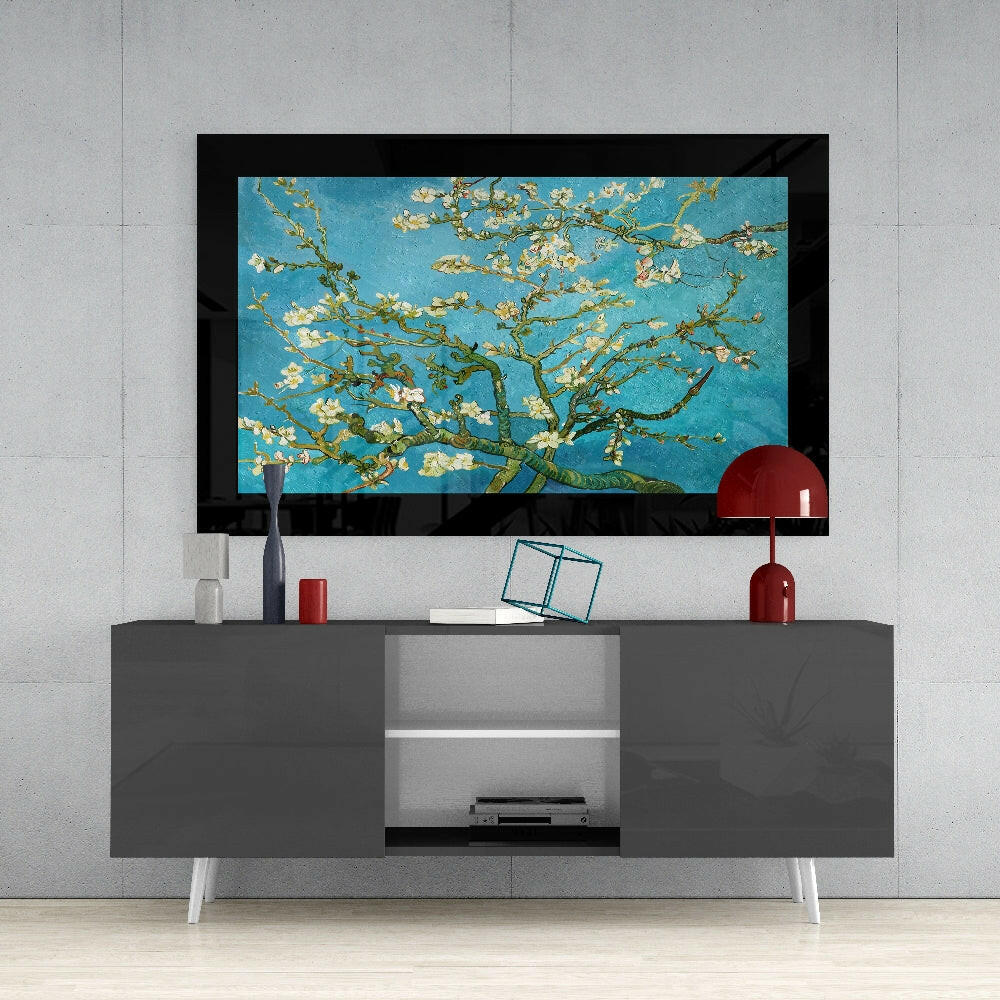 Framed turquoise glass art featuring white almond blossoms and green branches displayed above a gray media console with red accents.
