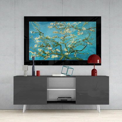 Framed turquoise glass art featuring white almond blossoms and green branches displayed above a gray media console with red accents.