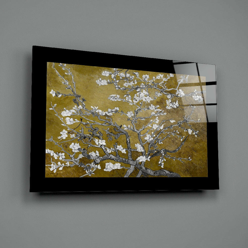 Black-framed glass wall art displaying gold and white almond blossoms branch, mounted on gray wall at angle.