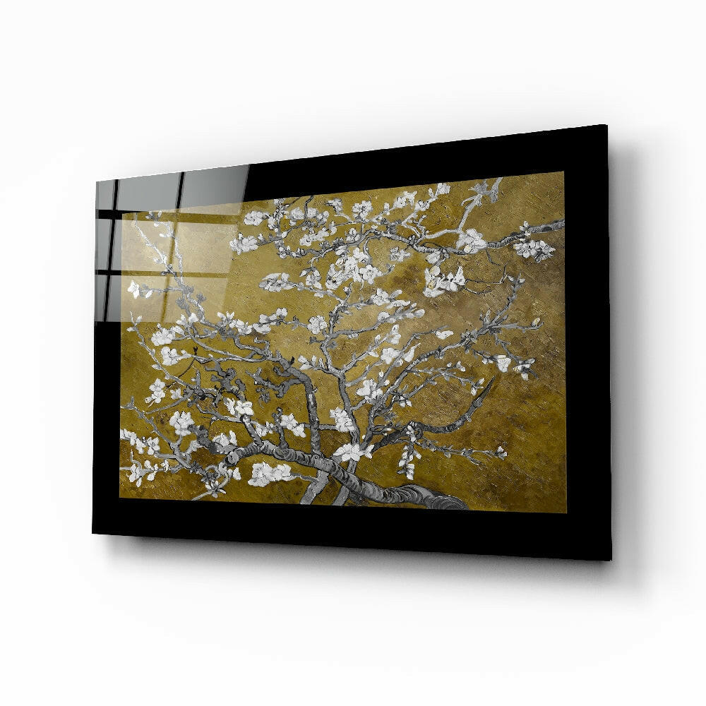 Black-framed glass wall art displaying white blossoming branches against a gold background, mounted at an angle.