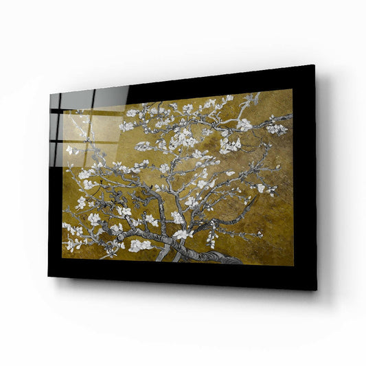 Black-framed glass wall art displaying white blossoming branches against a gold background, mounted at an angle.