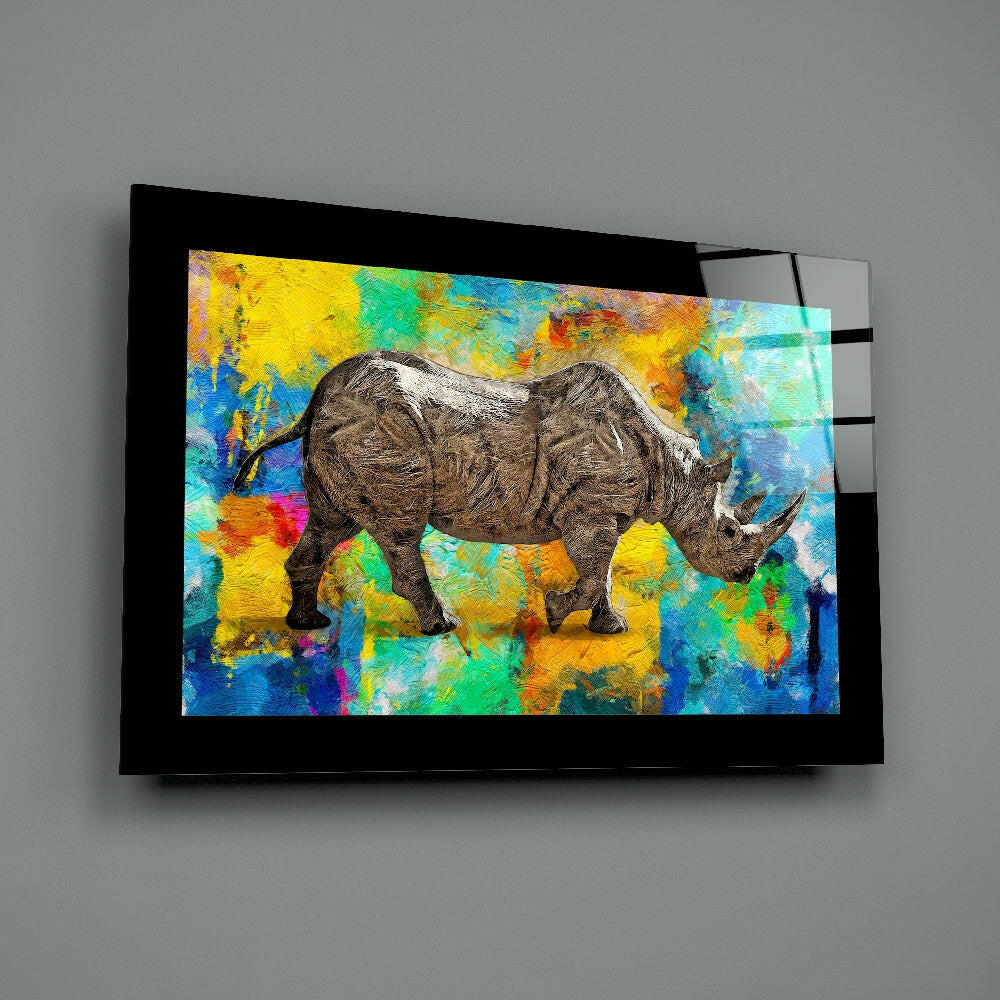 Black-framed glass wall art featuring a detailed rhinoceros against a vibrant multicolored abstract painted background, displayed at an angle on gray wall.