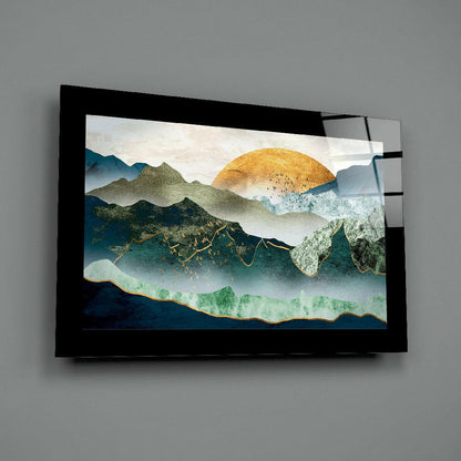 Black-framed glass wall art displaying layered mountains with golden sun, teal and green watercolor elements against gray wall.