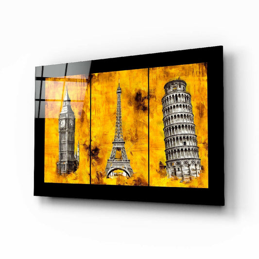 Black-framed glass wall art displaying three European landmarks—Big Ben, Eiffel Tower, and Leaning Tower of Pisa—against golden yellow textured backgrounds, mounted horizontally.
