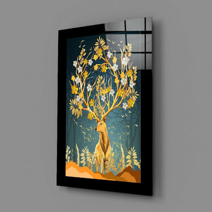 Black-framed glass wall art displaying a gold deer with flowering branches against a teal background, angled view showing depth and shadow.