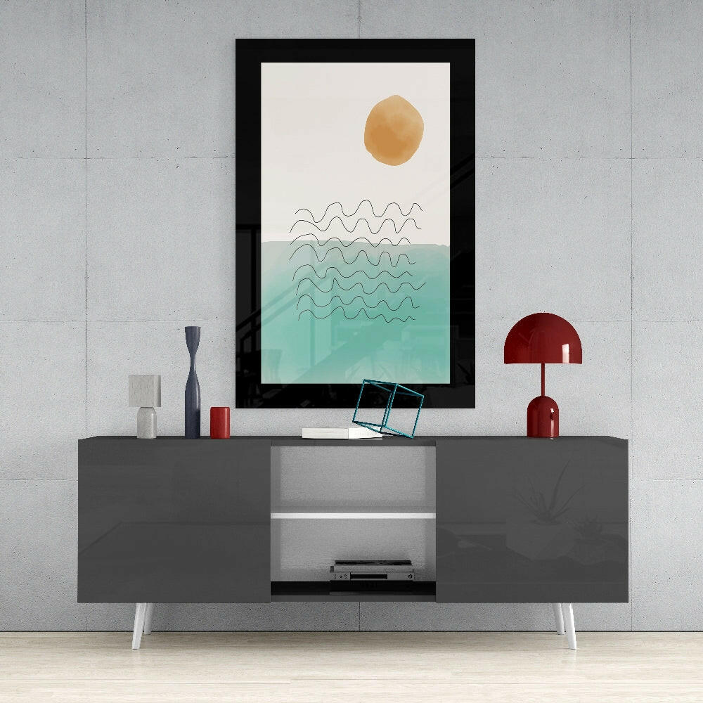 Framed minimalist seascape artwork with golden sun and turquoise waves displayed on gray media console with red lamp and accessories.