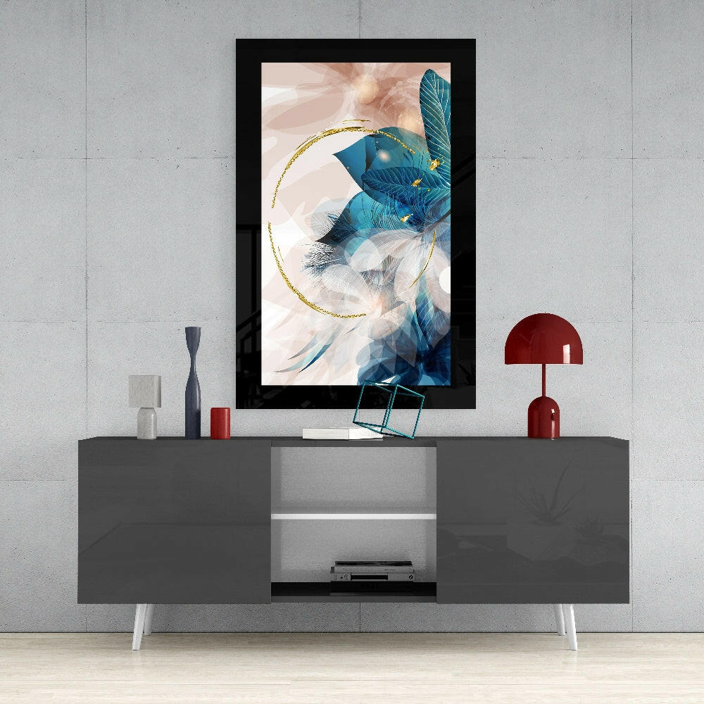 Black-framed abstract leaf glass wall art with blue feathers and gold circular accent displayed above gray media console.