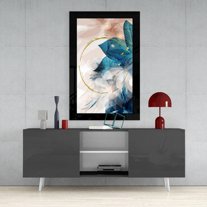 Black-framed abstract leaf glass wall art with blue feathers and gold circular accent displayed above gray media console.