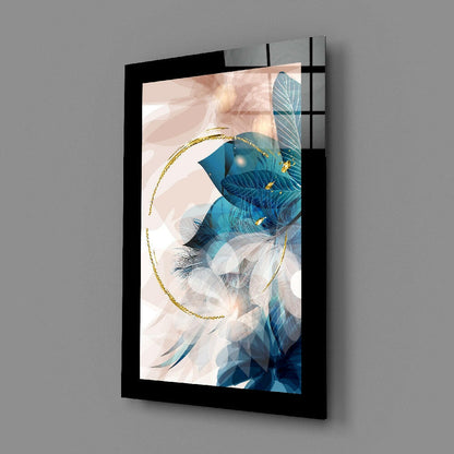 Black-framed glass wall art displaying abstract blue and teal leaves with gold circular accent, mounted on gray wall at angle.