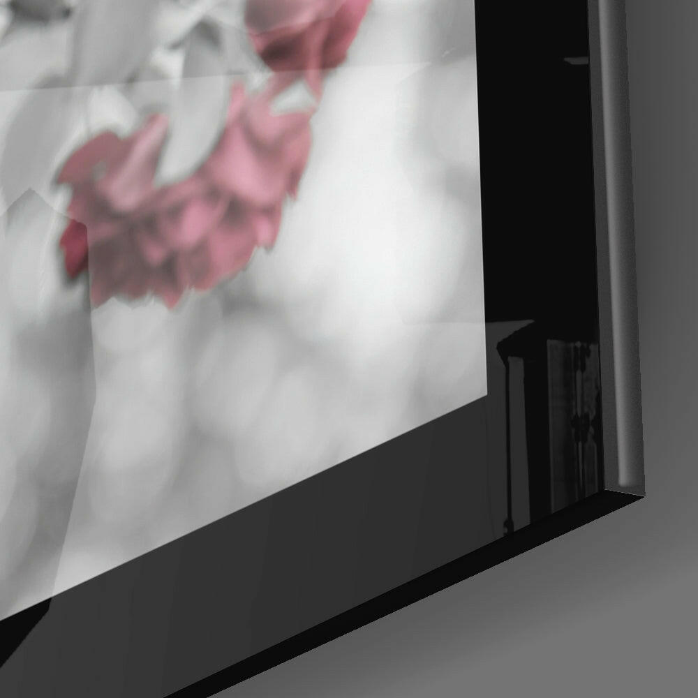 Close-up side angle of black-framed glass wall art displaying pink flowers on white background.
