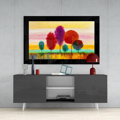Framed glass wall art depicting colorful trees in red, purple, orange, and teal against a gradient yellow and pink sky, displayed above a gray media console.