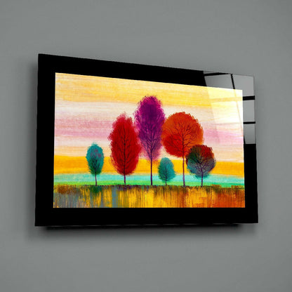 Framed glass wall art displaying five colorful trees in red, purple, orange, and teal against layered yellow, pink, and green sky and field.