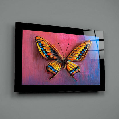 Angled view of black-framed glass wall art displaying a colorful orange and blue butterfly on a pink-to-blue gradient background.