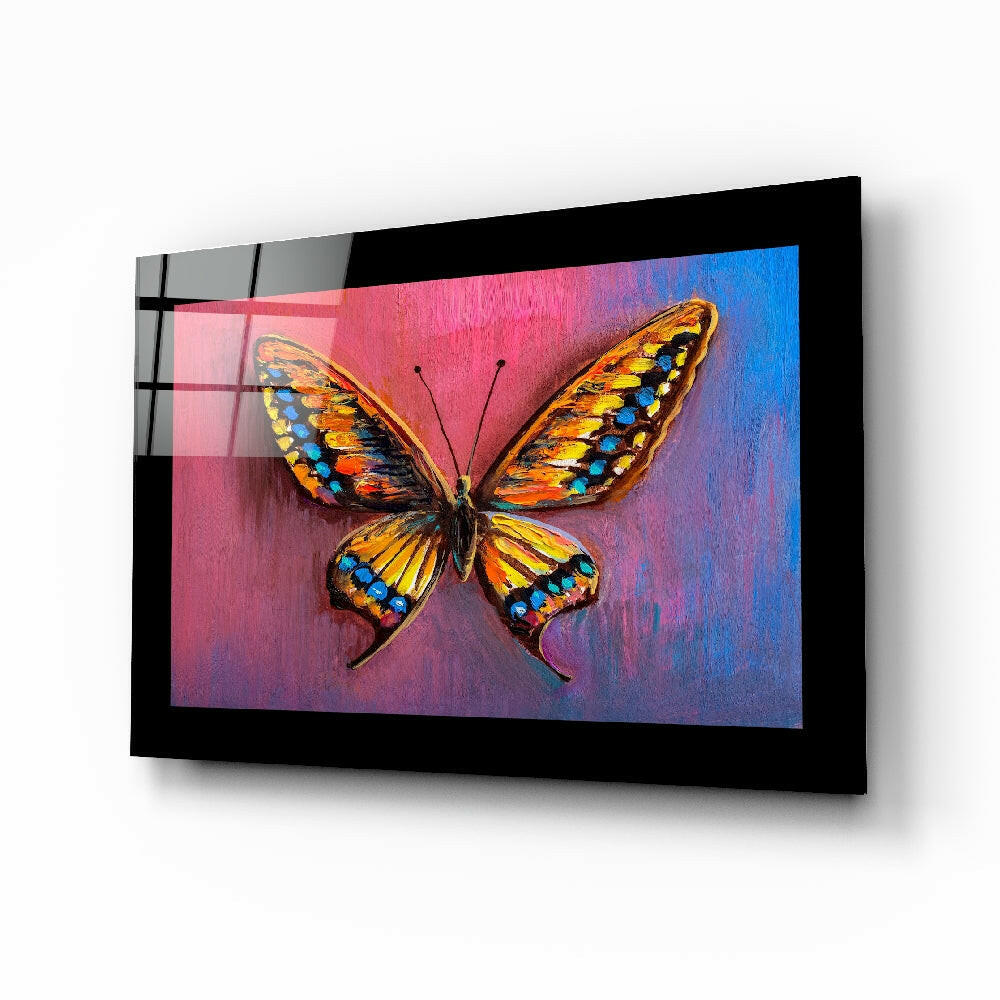 Black-framed glass wall art displaying a colorful butterfly with orange and yellow wings against a pink-to-blue gradient background, shown at an angle.