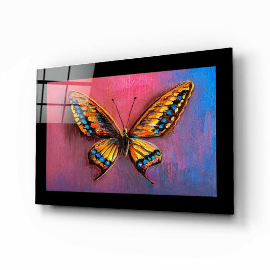 Black-framed glass wall art displaying a colorful butterfly with orange and yellow wings against a pink-to-blue gradient background, shown at an angle.