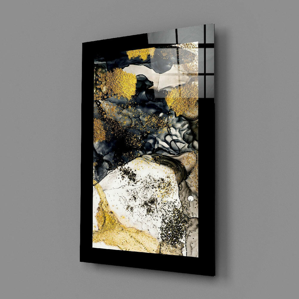 Black-framed glass wall art mounted on gray wall displaying abstract composition with gold, white, and dark gray powder textures and splatter effects.