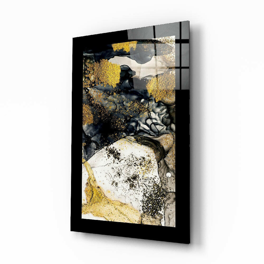 Black-framed glass wall art displaying abstract composition with gold leaf, white, grey, and black textured elements in angled perspective view.