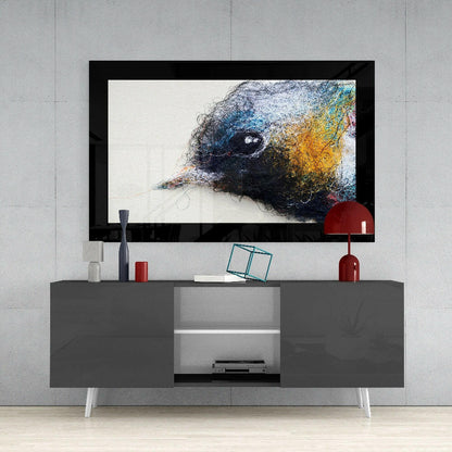 Framed colorful bird head glass art displayed on gray media console with red accessories and white legs against concrete wall.