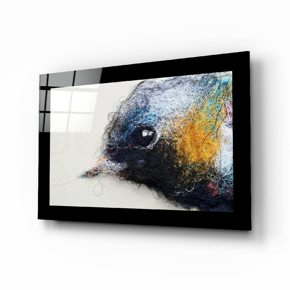 Black-framed glass wall art displaying a colorful abstract bird head in profile with blue, yellow, and dark threads on white background.