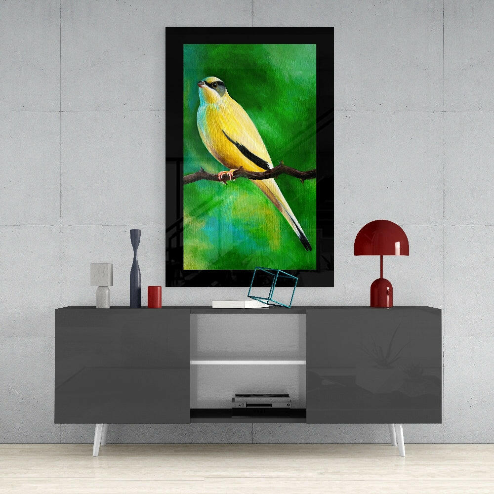 Yellow and green bird glass wall art with black frame displayed above gray media console with red lamp and accessories.