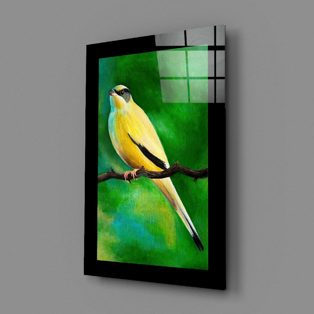Angled view of glass wall art featuring a yellow and black bird on a branch against a green gradient background, mounted in a black frame.