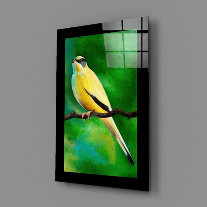 Angled view of glass wall art featuring a yellow and black bird on a branch against a green gradient background, mounted in a black frame.