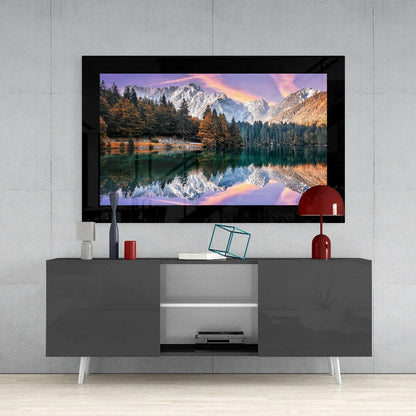 Glacier Lake Glass Wall Art displayed on a gray TV stand showing snow-capped mountains reflected in still water at sunset.