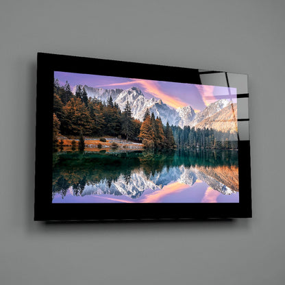 Black-framed glass wall art displaying a mountain lake landscape with snow-capped peaks, autumn forest reflection, and sunset sky, mounted on gray wall.