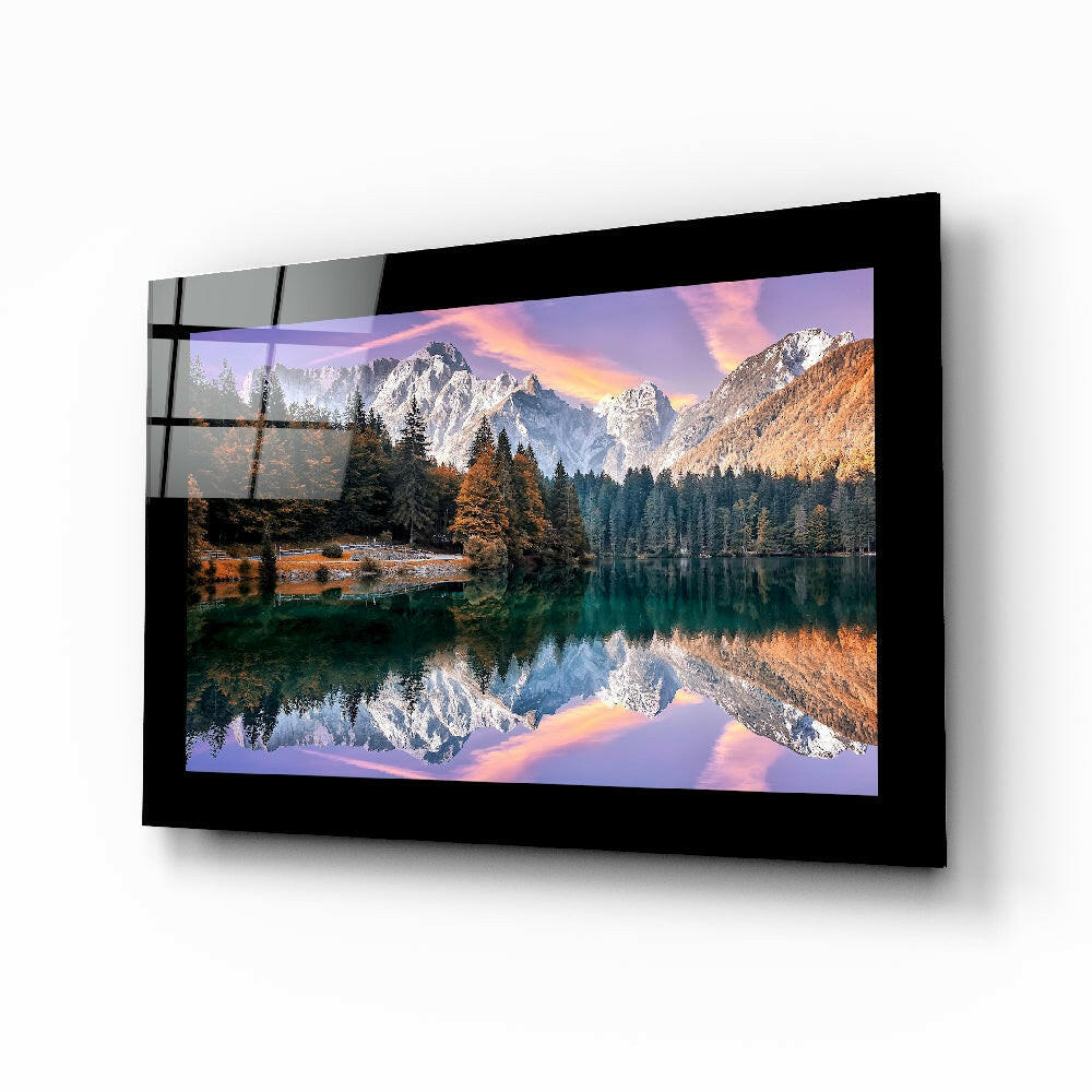 Black-framed glass wall art displaying a mountain lake landscape with snow-peaked peaks, autumn trees, and sunset reflection, mounted at an angle.