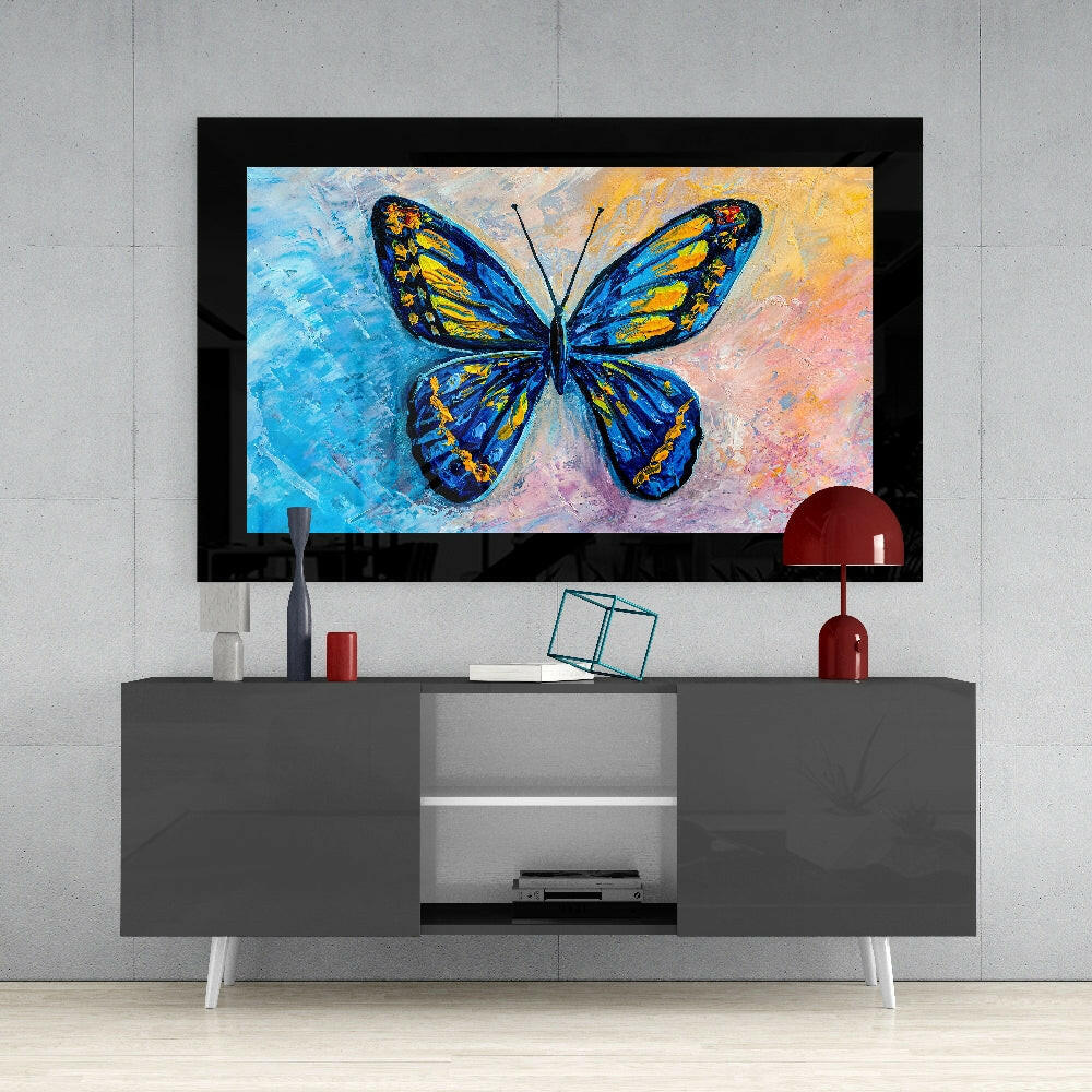 Colorful butterfly glass wall art with blue and yellow wings displayed above gray media console in modern living room setting.