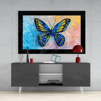 Colorful butterfly glass wall art with blue and yellow wings displayed above gray media console in modern living room setting.