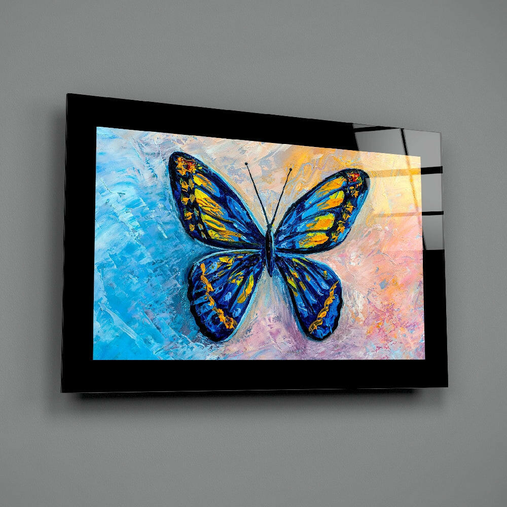 Black-framed glass wall art displaying a blue and yellow butterfly on a textured pastel background, mounted on gray wall.