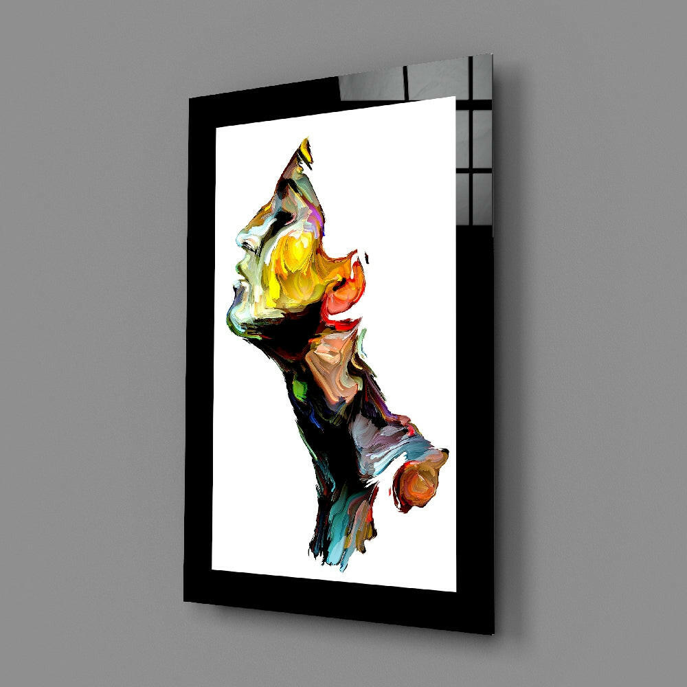 Black-framed glass wall art displaying an abstract colorful vertical composition with yellow, red, orange, and multi-hued brushstroke elements on white background, mounted at an angle against gray wall.