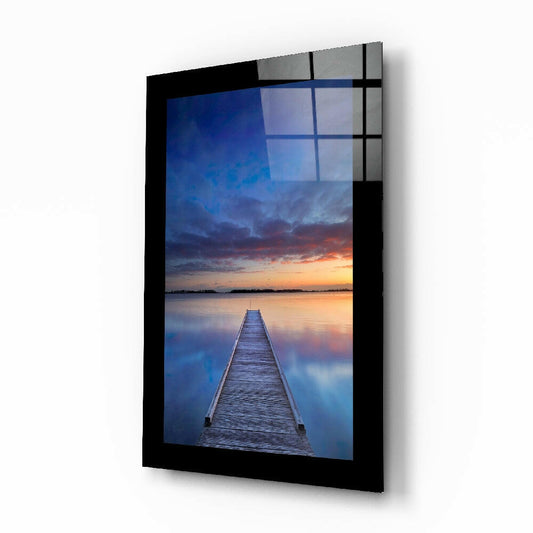 Black-framed glass wall art displaying a wooden jetty extending into a lake at twilight with blue and orange sky reflections.