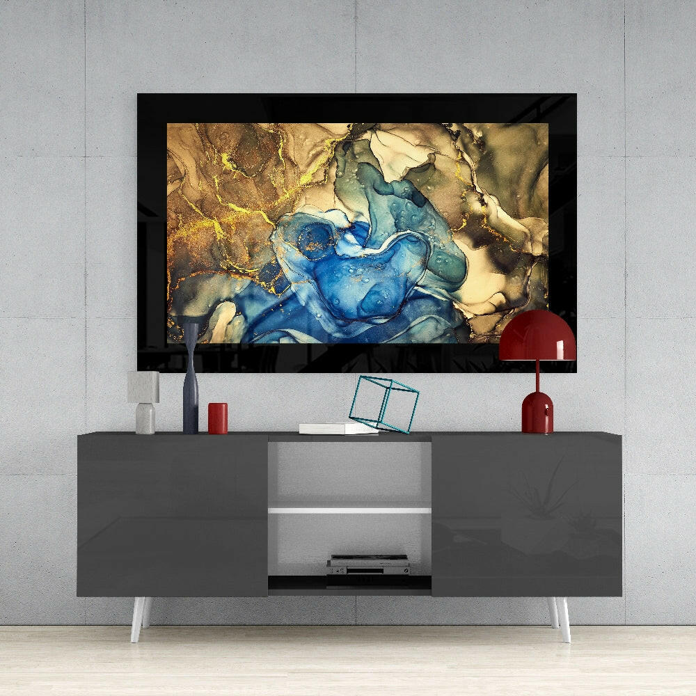 Framed abstract glass wall art with swirling blue and gold tones displayed above a gray media console in a modern living room setting.