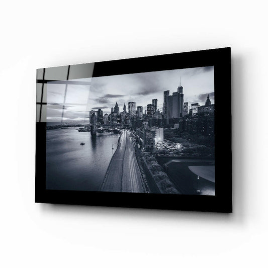 Black-framed glass wall art displaying monochromatic Manhattan skyline with highway and waterfront, mounted at angle on white background.