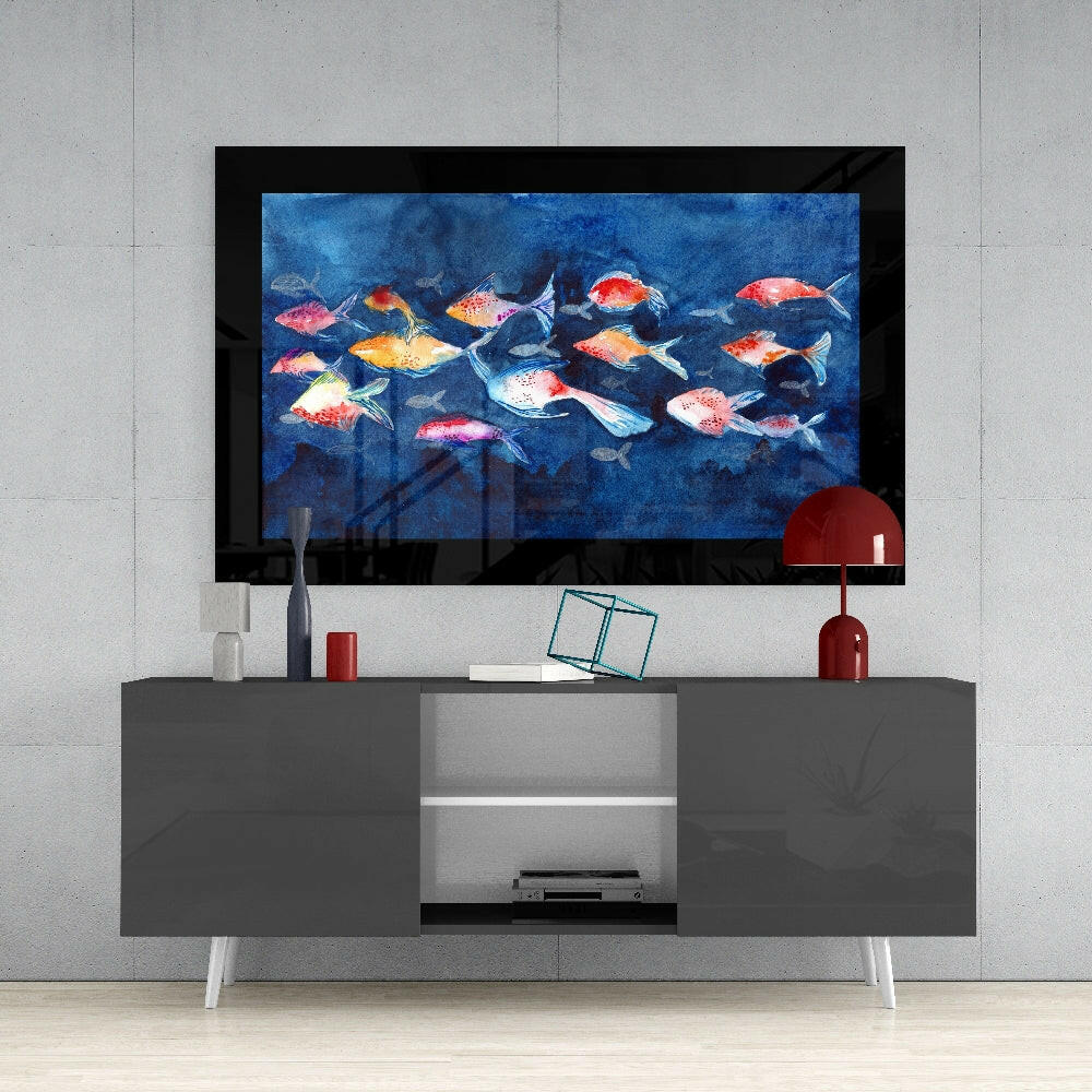 Colorful glass wall art displaying a school of red, orange, and white fish on blue background, mounted above a gray media console in a modern interior setting.