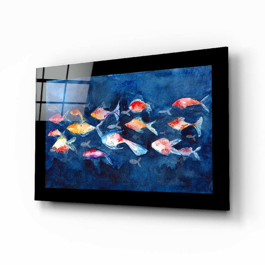 Black-framed glass wall art displaying a school of colorful red, orange, and white fish swimming against a deep blue underwater background, mounted at an angle.
