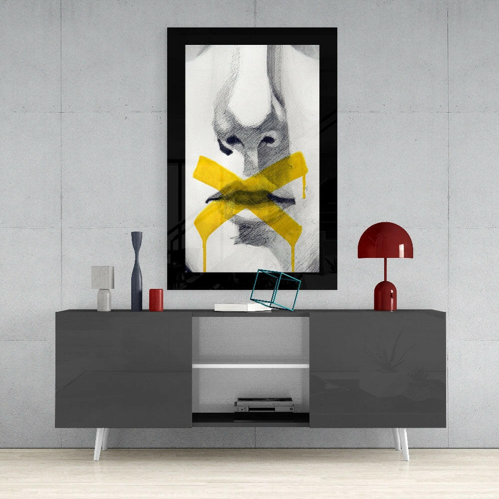 Black-framed wall art displaying pencil sketch of face with yellow bow, hung above gray media console with red lamp and accessories.