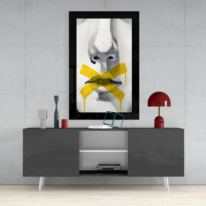 Black-framed wall art displaying pencil sketch of face with yellow bow, hung above gray media console with red lamp and accessories.