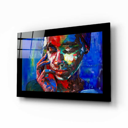Black-framed glass wall art displaying a colorful portrait of a person with red, blue, yellow, and green paint on their face against a blue background.