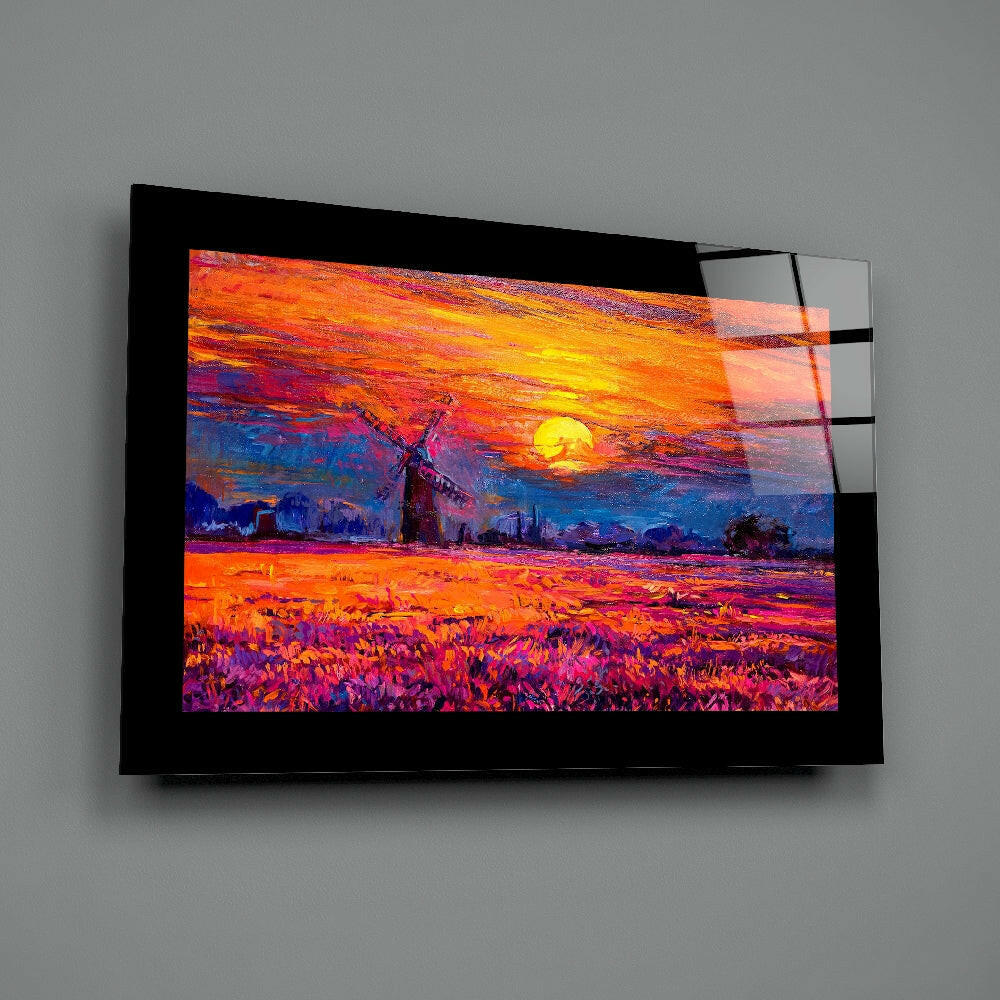 Black-framed glass wall art displaying a vibrant sunset landscape with windmill, mounted on gray wall at angle.