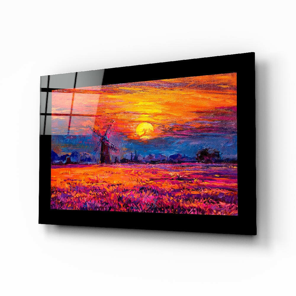 Black-framed glass wall art displaying a vibrant sunset landscape with golden sun, orange sky, and purple field with windmill, mounted on white wall.