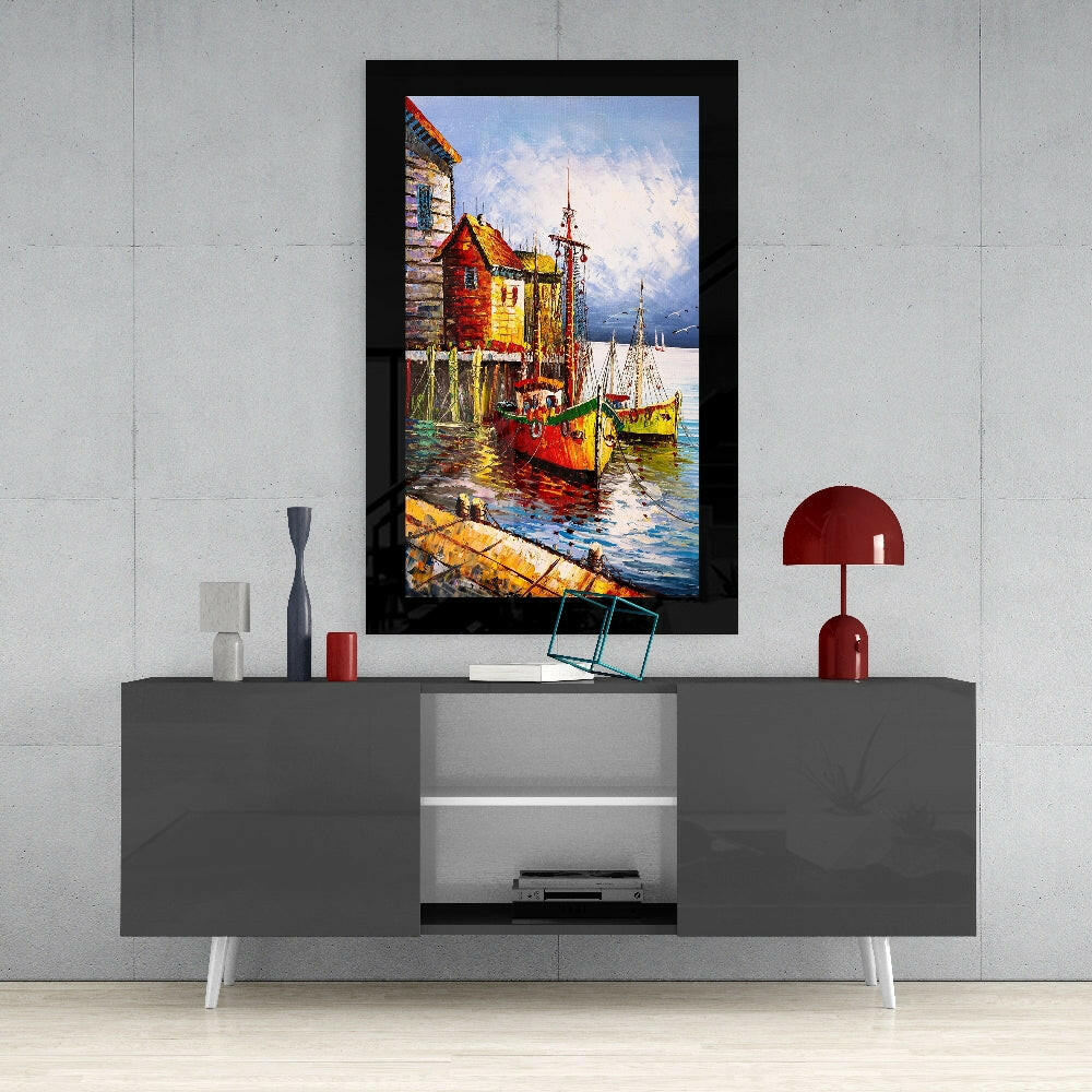 Framed glass wall art depicting colorful fishing boats and red-roofed buildings by water, displayed above gray media console in modern interior.