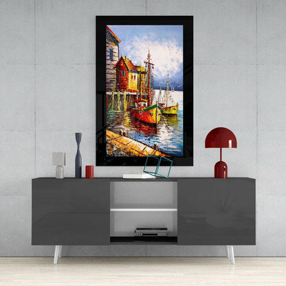 Framed glass wall art depicting colorful fishing boats and red-roofed buildings by water, displayed above gray media console in modern interior.