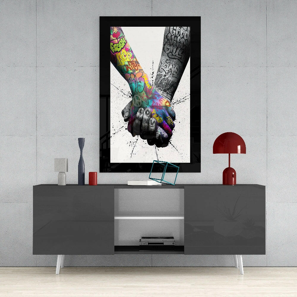 Framed artwork displaying two tattooed arms joining hands with colorful graffiti and black ink designs against white background, mounted above gray media console.
